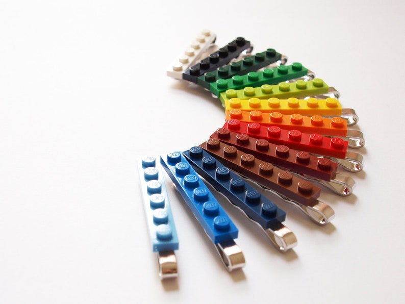 May include: A set of 12 colorful hair clips made from LEGO bricks. The clips are arranged in a rainbow pattern, with each clip featuring a different color.