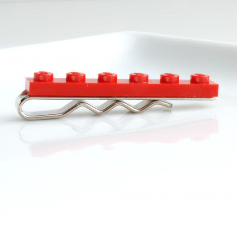 May include: A red Lego tie clip with a silver metal clasp. The tie clip is made of six Lego bricks.