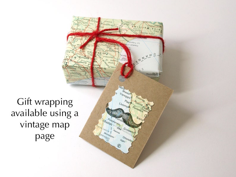 K&ouml;nnte beinhalten: Ein Geschenk, verpackt in einer Vintage-Landkarte, mit rotem Garn gebunden. Ein Anh&auml;nger in Form einer Karte mit einem Schnurrbart-Motiv ist angebracht. Der Text "Gift wrapping available using a vintage map page" ist sichtbar.