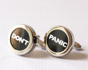 May include: A pair of silver cufflinks with black backgrounds. One cufflink says "DON'T" and the other says "PANIC".