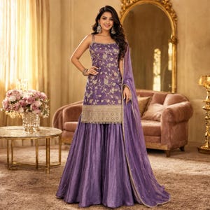 May include: A purple sleeveless kurta with intricate gold floral embroidery and a wide gold border, paired with matching wide-leg sharara trousers and a sheer purple dupatta with a gold trim, creating a coordinated three-piece ethnic ensemble.
