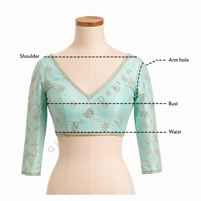 May include: A light turquoise blouse with a V-neck and long sleeves, adorned with gold embroidery. The garment is displayed on a mannequin, with labels indicating shoulder, armhole, bust, and waist measurements. The text "Gift City Design" is visible.