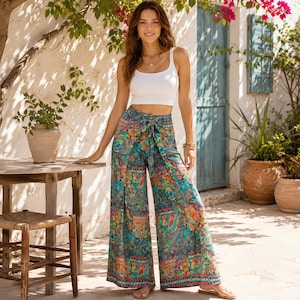 Puede incluir: Un top corto blanco sin mangas combinado con pantalones de tiro alto y pernera ancha, con un estampado floral y geométrico multicolor en tonos turquesa, naranja y amarillo, que incluye un lazo de tela a juego en la cintura.