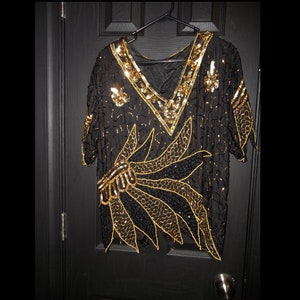 May include: A black and gold sequined top with a V-neck and short sleeves. The top features a large gold and black floral design.
