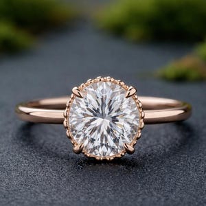 Puede incluir: Anillo de compromiso de oro rosa con un diamante de talla ovalada. El diamante está engastado en un bisel con cuentas. La banda del anillo es lisa y pulida, creando un aspecto clásico y elegante. Una joya para una promesa.