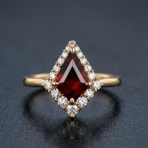 May include: A gold ring featuring a kite-shaped deep red garnet gemstone at the center, surrounded by a halo of small round white diamonds. The band is made of polished yellow gold, providing a clear contrast to the dark red stone.
