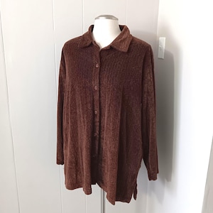 Op de afbeelding: Een bruin overhemd met lange mouwen en knopen. Het overhemd heeft een kraag en een textuurstof. Het wordt getoond op een mannequin tegen een witte en lichtgrijze achtergrond.