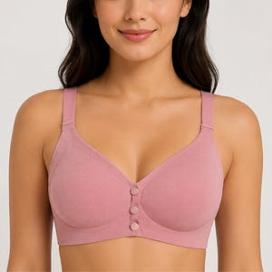 Op de afbeelding: Een stoffige roze beha met een geribbelde textuur en verstelbare bandjes. De voorkant heeft drie kleine, ronde knopen. De beha heeft een klassiek ontwerp met een comfortabele pasvorm, geschikt voor dagelijks gebruik.