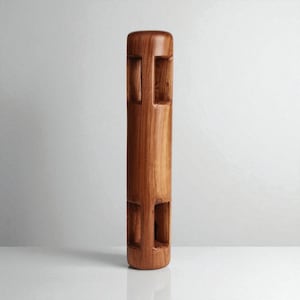 May include: A tall, cylindrical wooden sculpture with a warm brown finish. The sculpture features rectangular cutouts arranged vertically along its length. The piece stands upright against a neutral background, showcasing its carved details.