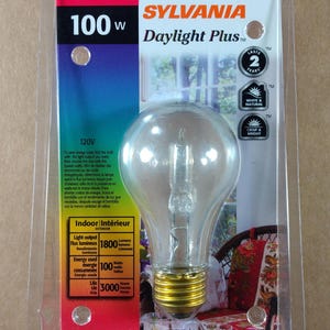 May include: A clear Sylvania Daylight Plus A19 light bulb in its original packaging. The package displays the bulb's specifications, including 100 watts, 1800 lumens, and a lifespan of 3000 hours. The packaging also indicates the bulb lasts for 2 years.