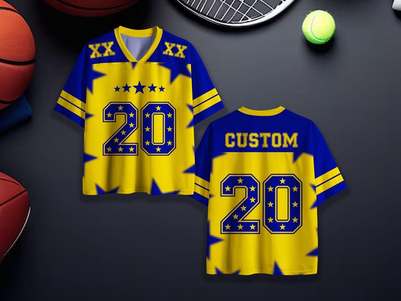 Puede incluir: Dos camisetas deportivas amarillas y azules con el n&uacute;mero 20. La parte delantera de la camiseta tiene el n&uacute;mero 20 en un contorno azul con estrellas. La parte trasera de la camiseta dice "CUSTOM" y tambi&eacute;n tiene el n&uacute;mero 20.