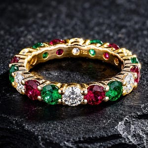 Peut inclure: Une alliance en or ornée d'un motif alterné de rubis rouges, d'émeraudes vertes et de diamants blancs ronds. L'anneau en métal porte le poinçon 750, indiquant de l'or 18 carats, et présente un design circulaire continu sur tout le pourtour.