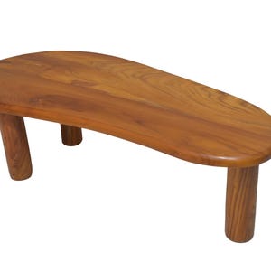 May include: A wooden coffee table with a natural finish. The table has a smooth, oval-shaped top and four short, rounded legs. The wood grain is visible, giving it a warm, inviting look. This piece is suitable for a living room or lounge area.