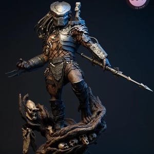 May include: A detailed 3D-printed Predator figure, standing on a base of skulls and tree roots. The figure is clad in armor and holds a spear and wrist blades. The figure has a metallic helmet and dreadlocks. The base has the text "KYLEVERSESTUDIO".