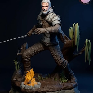 Puede incluir: Estatua impresa en 3D de un personaje de la serie The Witcher. La figura está en una pose dinámica, sosteniendo una espada, con una fogata a sus pies. La estatua es marrón y gris, con un fondo azul oscuro. El texto "KYLE VERSE STUDIO 3D PRINT" es visible.