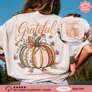 Puede incluir: Camiseta color crema con un diseño de calabaza colorida y la palabra "Grateful" en escritura naranja. La calabaza está decorada con varios patrones y rodeada de hojas de otoño. Adecuada para el otoño.
