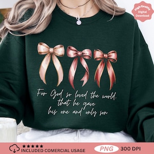 Pode incluir: Camisola verde escuro com três laços em aquarela em tons de rosa e dourado. O texto diz: "Porque Deus amou o mundo de tal maneira que deu o seu Filho unigénito". Download digital de alta qualidade.