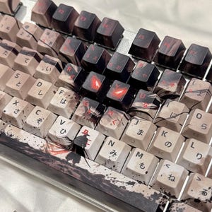 May include: Custom mechanical keyboard with keycaps featuring a black and white anime-inspired design. The keycaps have Japanese characters and red accents. The keyboard has a silver frame.