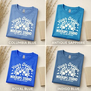 May include: Four folded t-shirts in different shades of blue: Columbia Blue, Antique Sapphire, Royal Blue, and Indigo Blue. Each shirt has a white graphic with the text "Your Design" and "MOCKUPS STUDIO High-Quality Mockups".