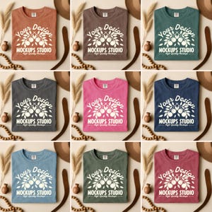 Puede incluir: Se muestran nueve camisetas dobladas en varios colores, incluyendo marrón, verde y rosa. Cada camiseta presenta el texto blanco "Your Design MOCKUPS STUDIO High-Quality Mockups". Las camisetas están dispuestas sobre un fondo neutro con elementos decorativos.