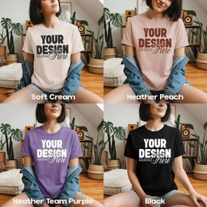 May include: Four t-shirts in different colors: soft cream, heather peach, heather team purple, and black. Each shirt has the text "YOUR DESIGN Here" in a contrasting color. The shirts are short-sleeved.