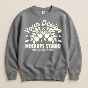 May include: A gray crewneck sweatshirt with white text that reads "Your Design" above "MOCKUPS STUDIO" and "High-Quality Mockups". The design includes a branch with leaves and fruit. The sweatshirt has ribbed cuffs and hem.