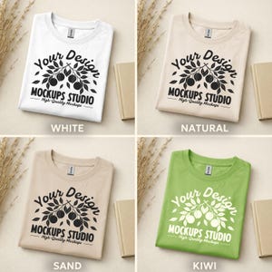 May include: Four folded t-shirts in white, natural, sand, and kiwi green. Each shirt features a graphic with the text "Your Design MOCKUPS STUDIO High-Quality Mockups". The shirts are displayed with small beige books and dried plants.