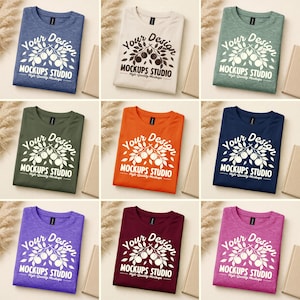 May include: Nine different colored t-shirts are displayed, each folded neatly. The shirts are various colors, including blue, white, green, orange, navy, purple, burgundy, and pink. Each shirt has the text "Your Design" and "MOCKUPS STUDIO" printed on it.
