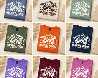 Puede incluir: Se muestran nueve camisetas plegadas de varios colores: azul, blanco, verde, naranja, marino, morado, burdeos y rosa. Cada camiseta tiene el texto "Your Design" y "MOCKUPS STUDIO" impreso en blanco.
