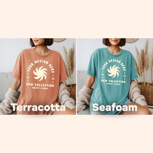 May include: Two short-sleeved t-shirts, one terracotta and one seafoam, each with a circular design that reads "YOUR DESIGN HERE" and "NEW COLLECTION SHEMET.STUDIO". The terracotta shirt is on the left, and the seafoam shirt is on the right.