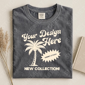 Może przedstawiać: Ciemnoszara koszulka z okrągłym dekoltem, z napisem "Your Design Here" i "New Collection!" w stylu vintage. Grafika z palmą jest wyśrodkowana pod tekstem. Widoczna jest również nazwa marki "SHEMET.STUDIO".