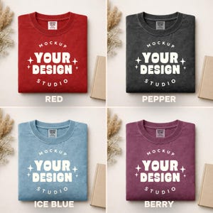 Peut inclure: Quatre t-shirts Comfort Colors de couleurs rouge, poivre, bleu glacier et baie. Chaque t-shirt affiche le texte "MOCKUP YOUR DESIGN STUDIO" en blanc. Les t-shirts sont pli&eacute;s et pr&eacute;sent&eacute;s avec des accessoires aux tons neutres.