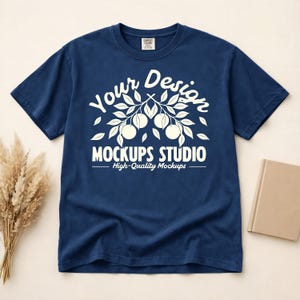 Può includere: Una maglietta blu navy con una grafica bianca. La grafica include le parole "Your Design" sopra un ramo con frutta e "Mockups Studio" sotto. Il testo "High-Quality Mockups" è sotto il testo dello studio.
