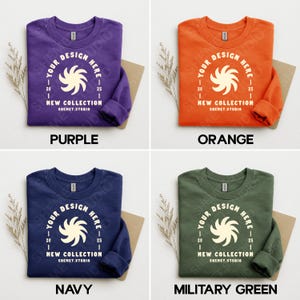 Puede incluir: Cuatro sudaderas de cuello redondo en morado, naranja, azul marino y verde militar. Cada sudadera presenta un dise&ntilde;o gr&aacute;fico blanco con el texto "YOUR DESIGN HERE" y "NEW COLLECTION" con el nombre de la tienda "SHEMET.STUDIO".