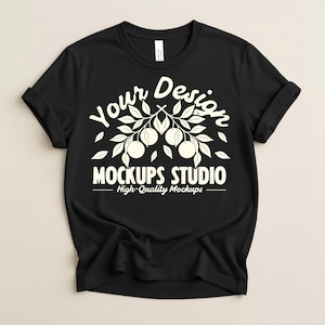 Könnte beinhalten: Schwarzes T-Shirt mit hochgekrempelten Ärmeln. Das Shirt zeigt ein weißes Grafikdesign mit dem Text "Your Design" über einem Ast mit Früchten und Blättern und "MOCKUPS STUDIO - High-Quality Mockups" darunter.