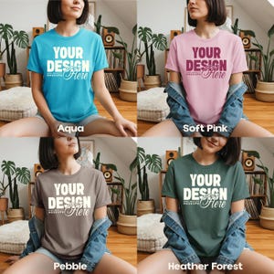 May include: Four t-shirts in aqua, soft pink, pebble, and heather forest colors. Each shirt has the text "YOUR DESIGN Here" in white. The shirts are displayed on a person sitting on a light-colored surface.