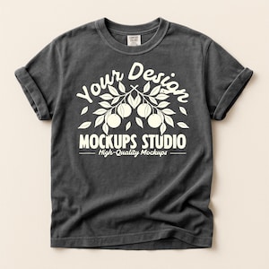 Può includere: T-shirt grigio scuro con maniche arrotolate. La maglietta presenta una grafica bianca con la scritta "Your Design" sopra un ramo con frutta e foglie, e "MOCKUPS STUDIO" sotto, con "High-Quality Mockups" sotto.