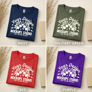 May include: Four t-shirts in navy, military green, red, and purple. Each shirt features a white graphic with the text "Your Design MOCKUPS STUDIO High-Quality Mockups". The shirts are displayed on a neutral background with a book and dried plants.