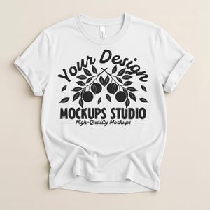 Könnte beinhalten: Weißes T-Shirt mit hochgekrempelten Ärmeln. Das Shirt zeigt ein schwarzes Grafikdesign mit dem Text "Your Design" über einem Ast mit Früchten und den Worten "MOCKUPS STUDIO - High-Quality Mockups" darunter.