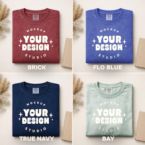Peut inclure: Quatre t-shirts de couleurs diff&eacute;rentes : rouge brique, bleu, marine et vert clair. Chaque t-shirt porte l'inscription blanche "MOCKUP YOUR DESIGN STUDIO". Les t-shirts sont pr&eacute;sent&eacute;s sur un fond neutre avec un livre et des plantes d&eacute;coratives.