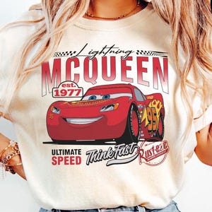 Puede incluir: Camiseta color crema con un dise&ntilde;o de Rayo McQueen de la pel&iacute;cula Cars. El dise&ntilde;o incluye el texto "Lightning McQueen", "est. 1977", "Ultimate Speed" y "Think Fast". El gr&aacute;fico es en rojo, blanco y negro.