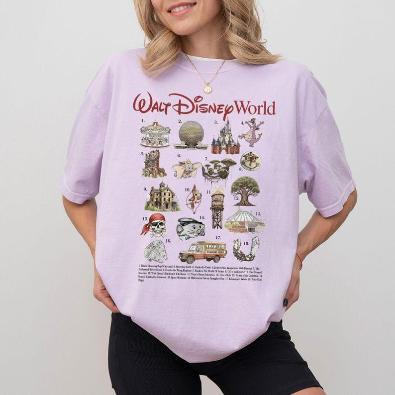 Puede incluir: Una camiseta de color lila claro con el texto "Walt Disney World" en escritura roja. La camiseta presenta un gr&aacute;fico con 18 ilustraciones de atracciones y personajes de Disney World, incluyendo el Castillo de Cenicienta y el &Aacute;rbol de la Vida.