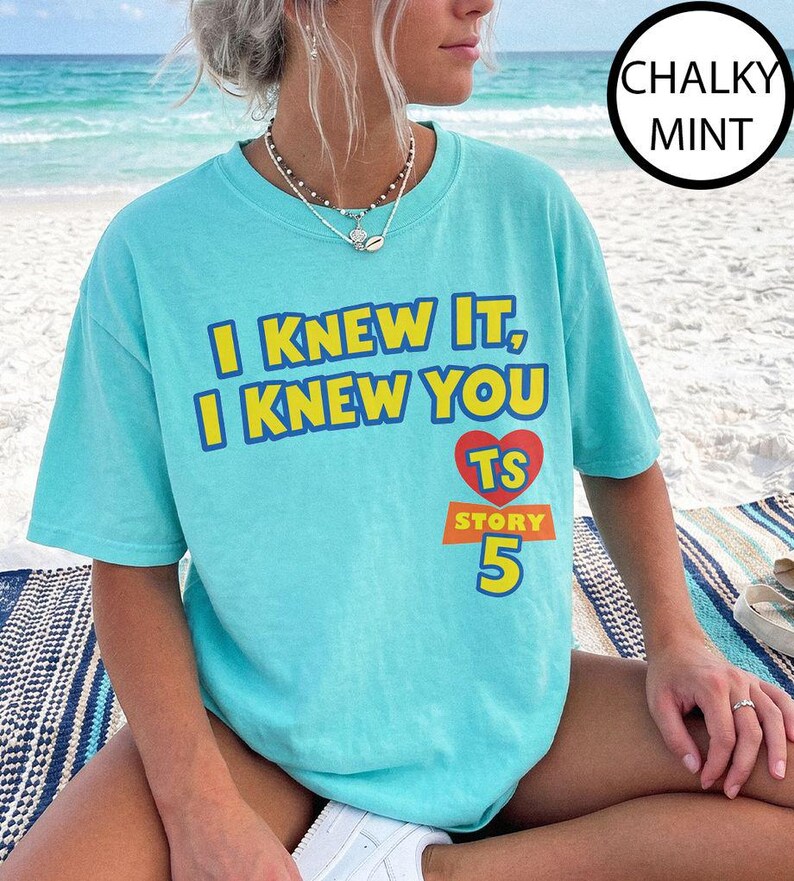 May include: A chalky mint short-sleeve t-shirt featuring the yellow text I KNEW IT, I KNEW YOU above a red heart containing the letters TS, with the word STORY and the number 5 printed in yellow below the heart on a rectangular orange background.