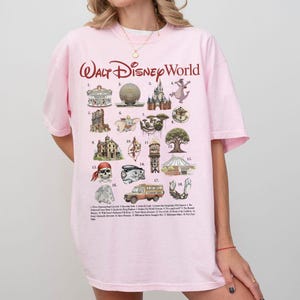 Puede incluir: Una camiseta rosa claro con la inscripci&oacute;n "Walt Disney World" en cursiva. La camiseta muestra varios iconos y atracciones de Disney World, incluyendo un carrusel, Spaceship Earth y un castillo. La camiseta es de estilo casual.