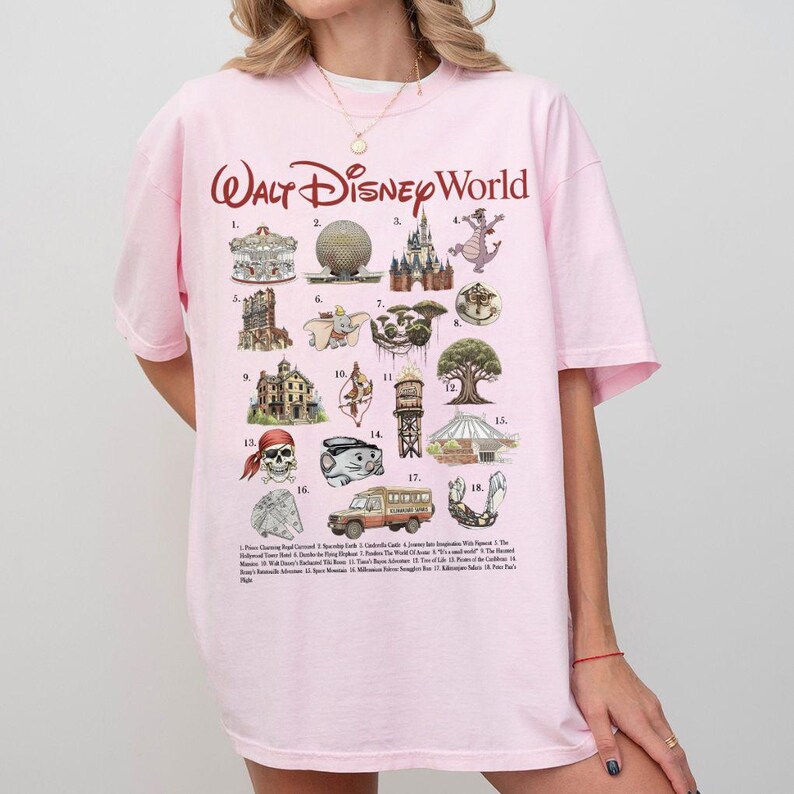Puede incluir: Una camiseta rosa claro con la inscripci&oacute;n "Walt Disney World" en cursiva. La camiseta muestra varios iconos y atracciones de Disney World, incluyendo un carrusel, Spaceship Earth y un castillo. La camiseta es de estilo casual.