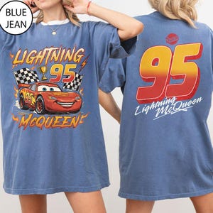 K&ouml;nnte beinhalten: Blaues T-Shirt mit Lightning McQueen-Motiv aus dem Film Cars. Auf der Vorderseite steht "Lightning 95 McQueen" mit einem Rennwagen, Zielflaggen und einer Troph&auml;e. Auf der R&uuml;ckseite steht "95 Lightning McQueen" in gro&szlig;en Buchstaben.