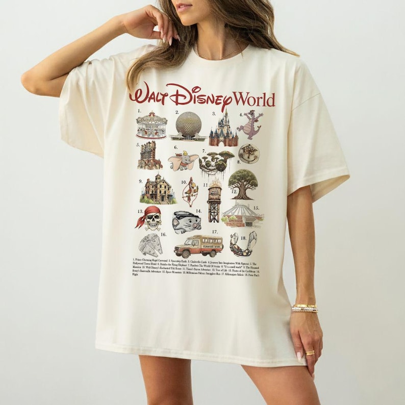 Puede incluir: Camiseta extragrande de color crema con un gr&aacute;fico de las atracciones de Walt Disney World. La camiseta incluye el texto "Walt Disney World" en rojo, con ilustraciones numeradas de varios puntos de referencia del parque.