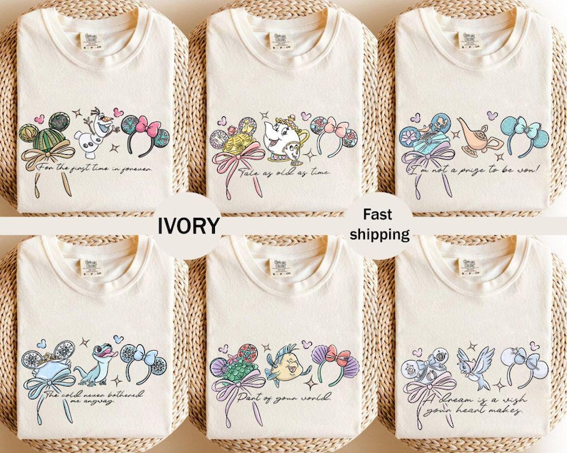 May include: Ivory-colored t-shirts with various Disney-themed designs. Each shirt features a different graphic, including characters and phrases like "For the first time in forever" and "Tale as old as time." The shirts have a crew neck.