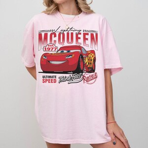 Puede incluir: Una camiseta rosa claro con un dise&ntilde;o de Rayo McQueen de la pel&iacute;cula Cars. El dise&ntilde;o incluye el texto "Lightning McQueen est. 1977", "Ultimate Speed", "Think Fast" y "Rust-eze".