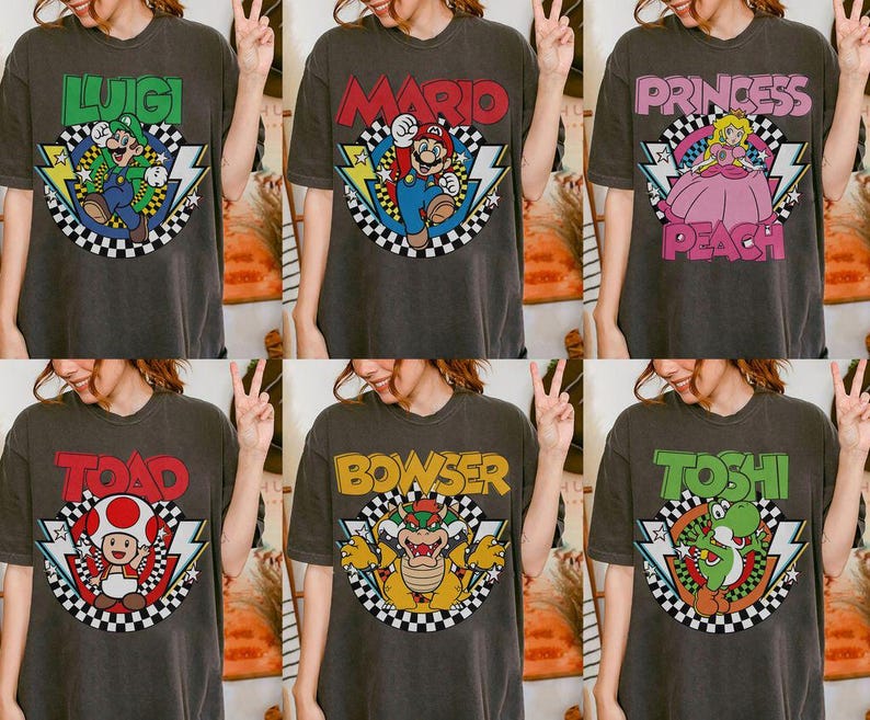 May include: A charcoal gray t-shirt featuring a graphic print of a Nintendo character. The design includes the character's name in bold letters, a checkered circle, and lightning bolt accents. Characters include Luigi, Mario, Princess Peach, Toad, Bowser, and Yoshi.